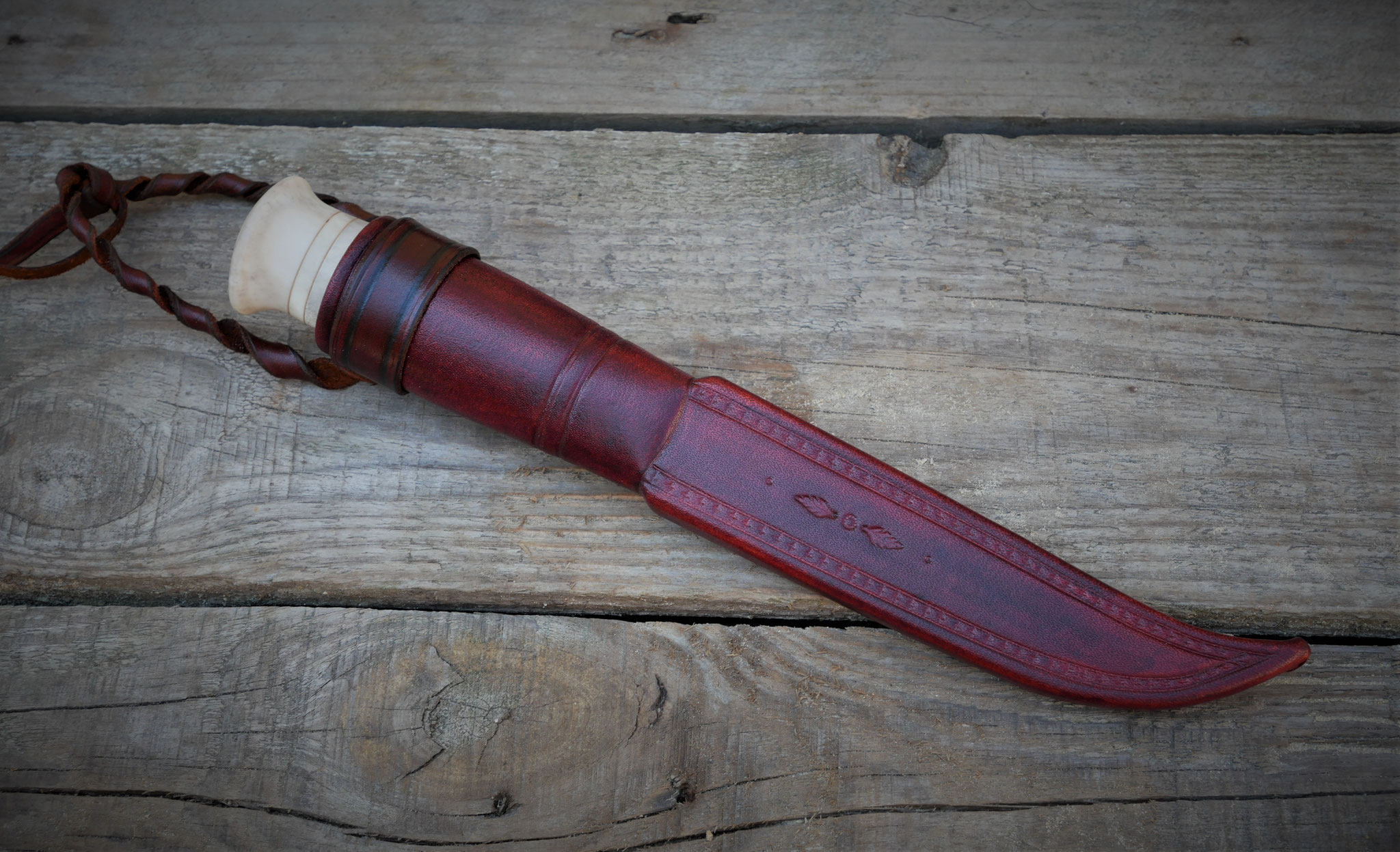 Puukko in verzierter roter Scheide auf Holz